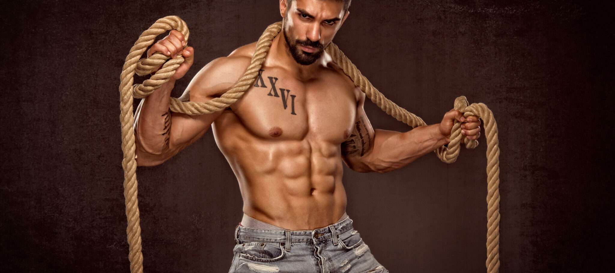 暗い背景にロープを保持している筋肉質の男性。