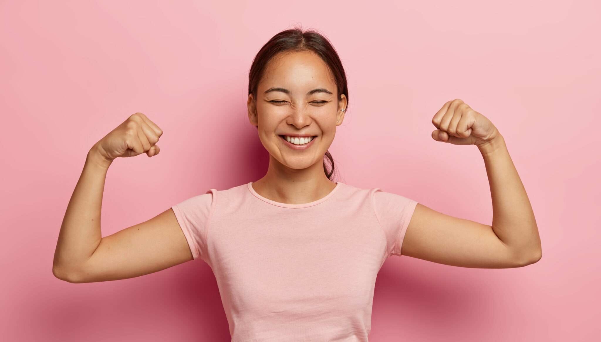 韓国のピンクの背景に筋肉を曲げるアジア系の若い女性。