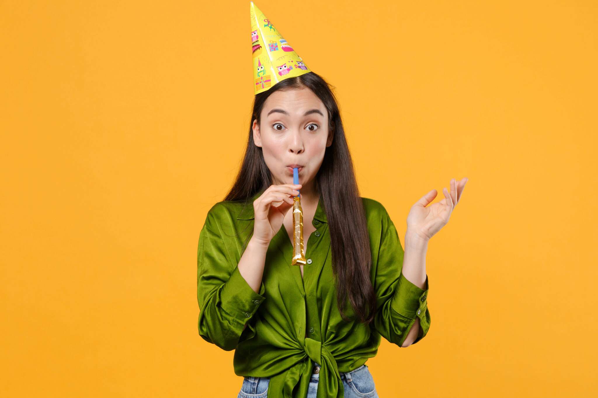 韓国の黄色の背景にパーティーハットをかぶって泡を吹く若い女性。