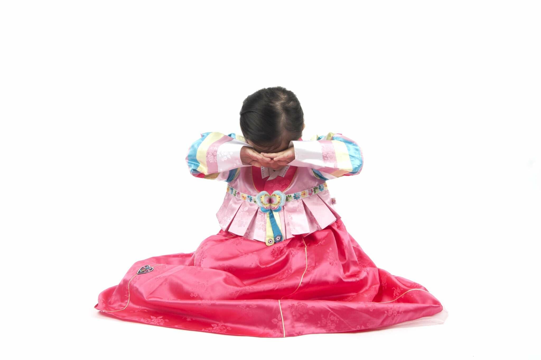 白い背景に韓服を着た小さな女の子が座っています。