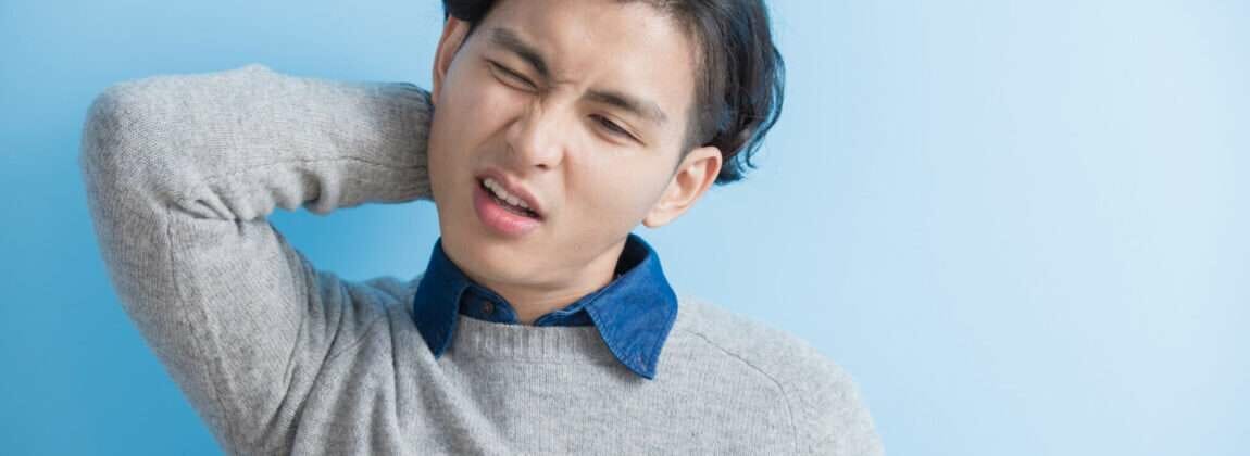 韓国の青い背景に首の痛みを持つ若い男性。 韓国の青い背景に首の痛みを持つ若い男性。