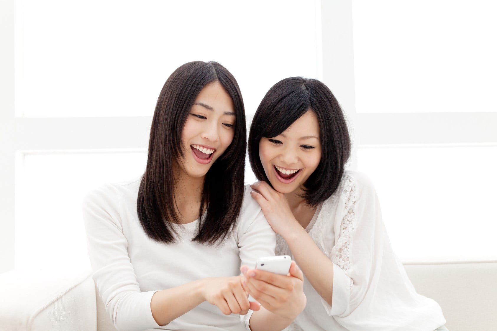 韓国出身のアジア人女性 2 人がソファに座って携帯電話を見ている。