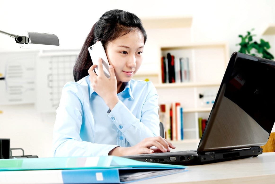韓国でノートパソコンの前で携帯電話で話す女性。