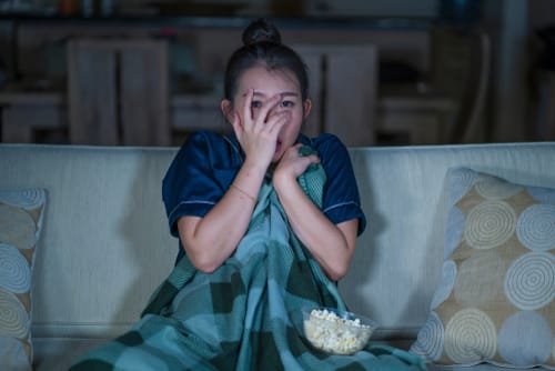 ポップコーンを膝に乗せてソファに座り、韓国映画マラソンを楽しむ女性。 ポップコーンを膝に乗せてソファに座り、韓国映画マラソンを楽しむ女性。