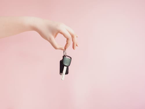韓国のピンクの背景に車のキーを持つ女性の手。 韓国のピンクの背景に車のキーを持つ女性の手。