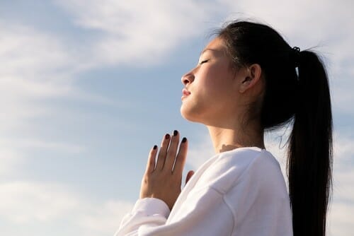韓国から来たアジア系の若い女性が青空の前で瞑想している。