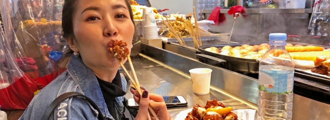 屋台でおいしい韓国料理を食べる女性。