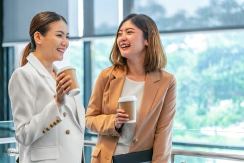 コーヒーカップを持ちながら笑う2人の韓国人ビジネスウーマン。