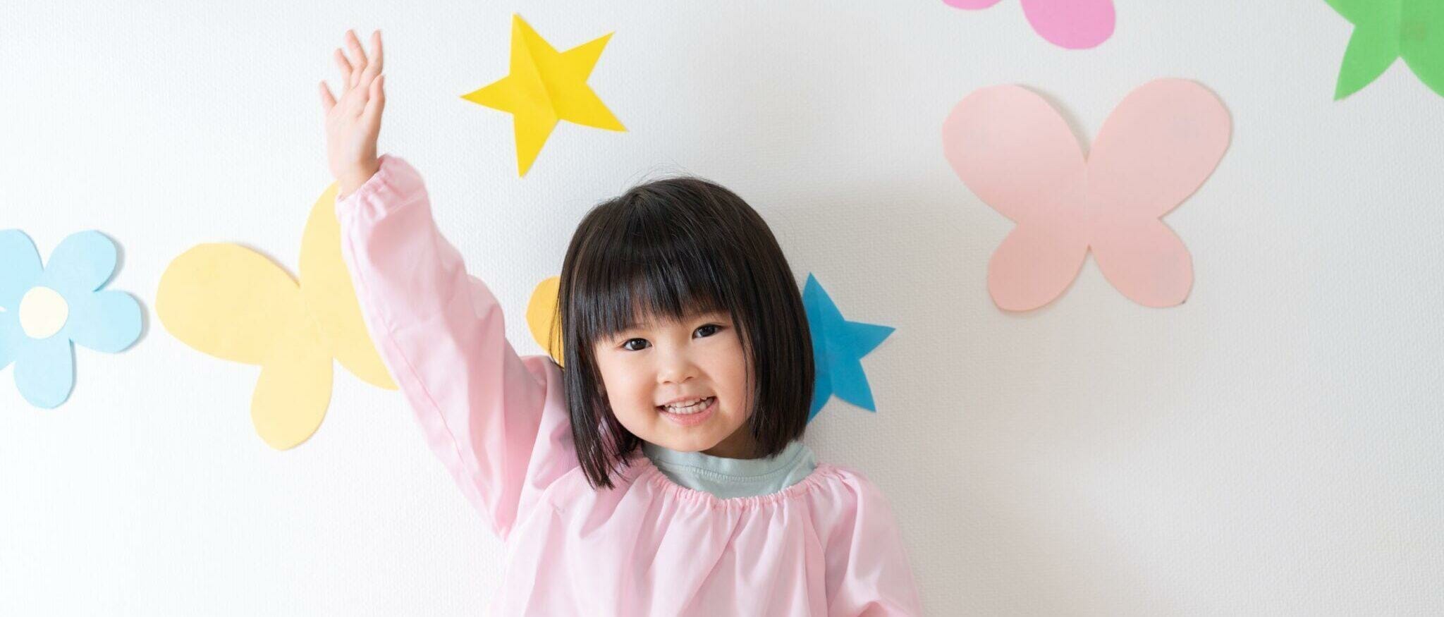 韓国の蝶でいっぱいの壁の前で腕を振るアジア人の少女。