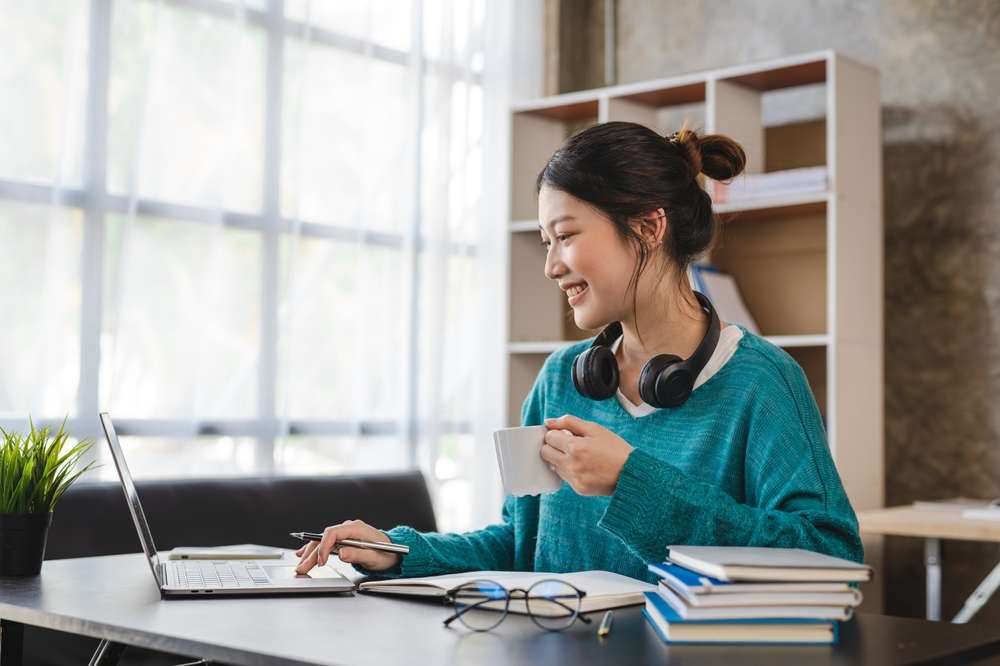 ノートパソコンとコーヒーを飲みながら自宅で働く韓国人女性。