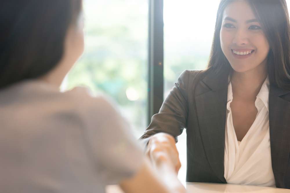 ビジネススーツを着た女性が韓国出身の別の女性と握手をしている。