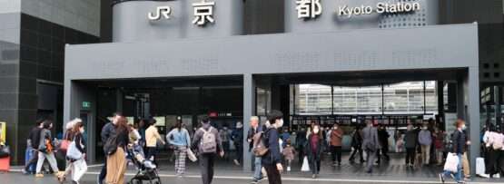 京都駅前を歩く人々。上には日本語と英語で「JR京都駅」と書かれた標識が見える。近くでは韓国語教室が韓国語学習に興味のある人を歓迎している。