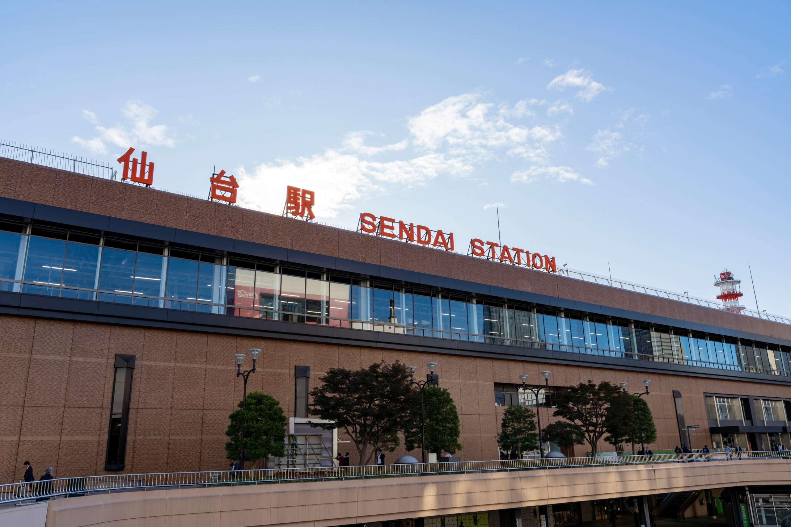 快晴の空を背景に、ビル屋上に大きな赤い看板が掲げられた仙台駅の外観。外を歩いている人はほんの数人で、おそらく仙台にある近くの韓国語教室に向かうのだろう。