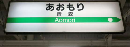 駅の標識には日本語と英語で「Aomori」と書かれており、その下に方向矢印が書かれている。その下には日本語の文字で「Aomori」と書かれている。