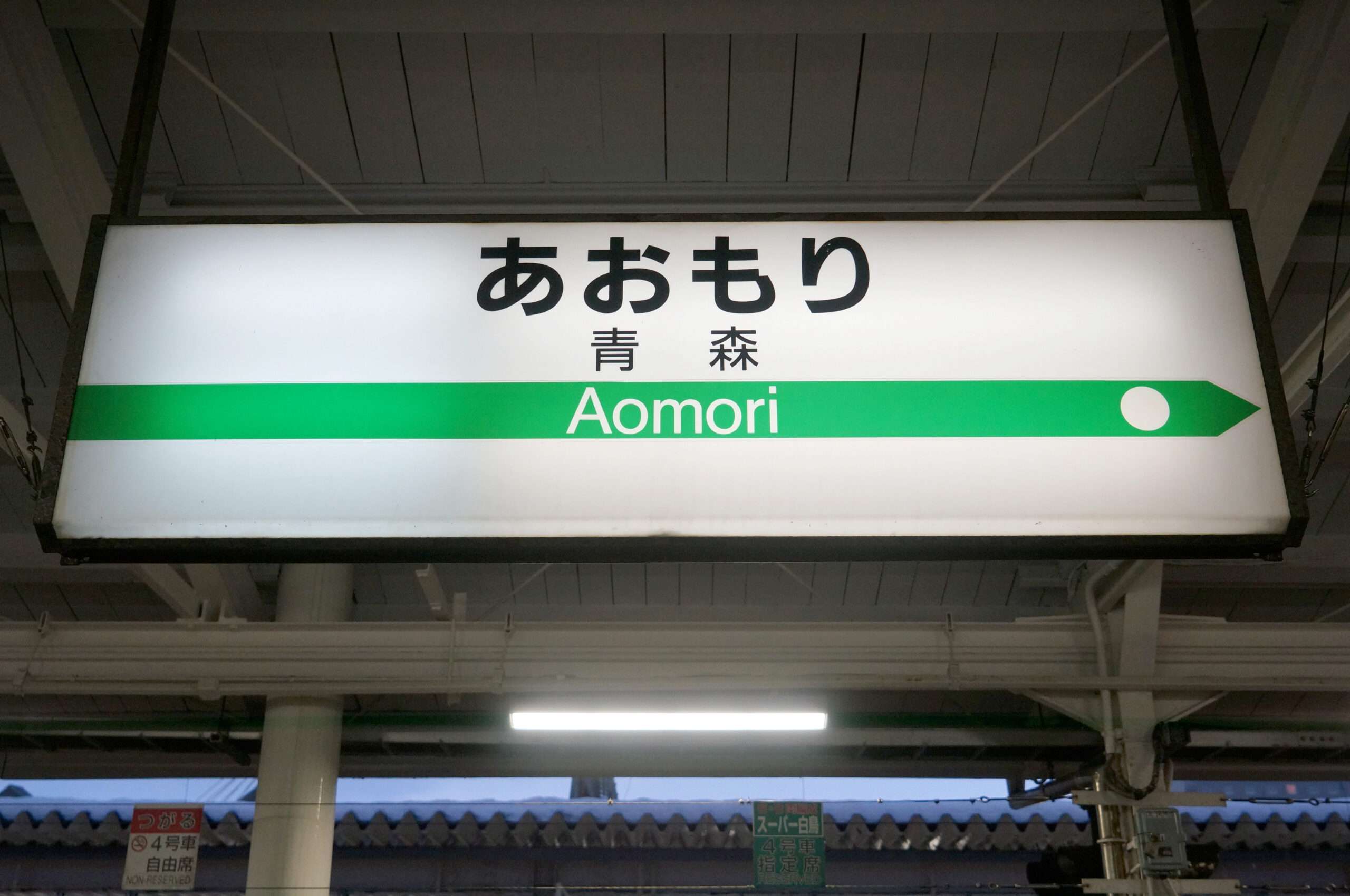 駅の標識には日本語と英語で「Aomori」と書かれており、その下に方向矢印が書かれている。その下には日本語の文字で「Aomori」と書かれている。