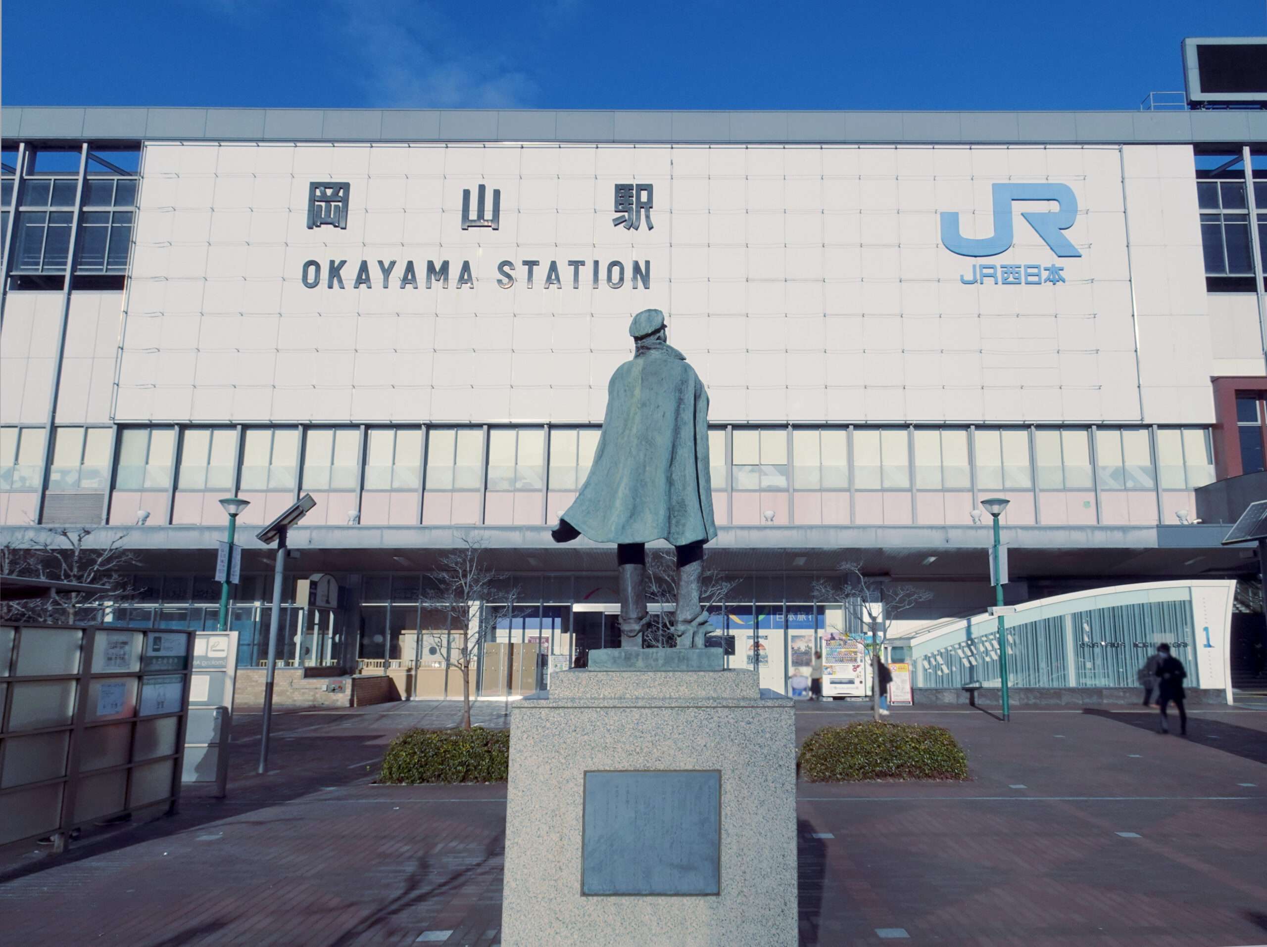 日本の岡山駅前には、大きな建物の正面に JR 西日本のロゴが大きく掲げられた銅像が立っています。近隣の岡山・倉敷地域は、世界中から語学愛好家が集まる韓国語教室など、文化体験で賑わっています。