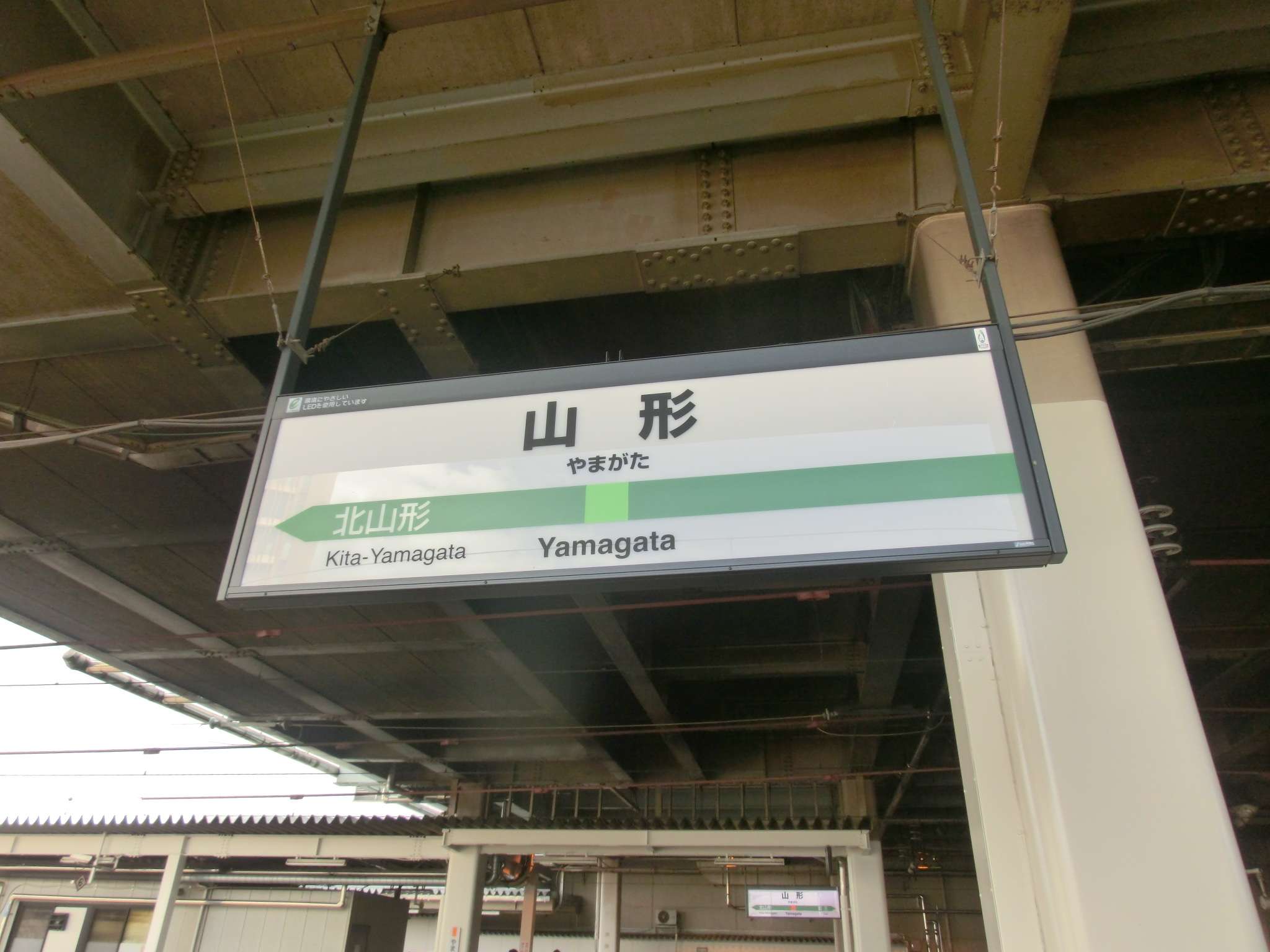 駅の標識には大きな金属製の天井の下に「山形」と「北山形」の文字が表示されており、山形・米沢の文化と、近くにある韓国語教室のような現代的な要素の融合を思い起こさせます。