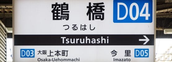 日本の鶴橋の駅標識は、D03 の大阪上本町と D05 の今里の間に位置する D04 への方向を示しています。近くには、個人に合わせた語学学習を提供する韓国語教室マンツーマンがあります。.