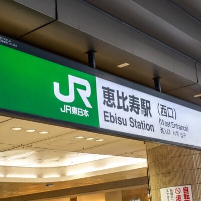 東京の恵比寿駅西口の看板。建物の天蓋の下に JR 東日本のロゴと場所の詳細が記載されています。近くには、個人向けの韓国語レッスンに興味のある方向けの韓国語教室マンツーマンもあります。.