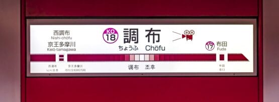 調布駅標識 KO18、西調布駅、京王多摩川駅、布田駅行きの案内が記載されています。背景は赤です。テキストは日本語と英語で書かれており、旅行者や近くの韓国語教室マンツーマンに通っている人に最適です。.