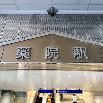 薬院駅の入口の看板の上には日本語の文字が誇らしげに表示されており、その下では人々がエスカレーターで上がっており、おそらく韓国語のマンツーマンレッスンへ向かっている。.