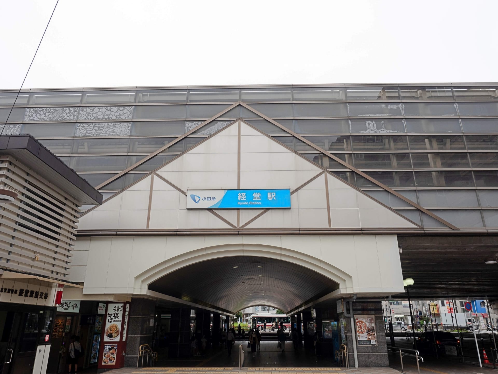 京成駅の外観は、印象的な三角屋根と入口上の青い看板が特徴で、賑やかな都市景観を背景に、経堂に通う人々が帰宅途中に韓国語教室のマンツーマンを探していたような場所を思い出させます。.