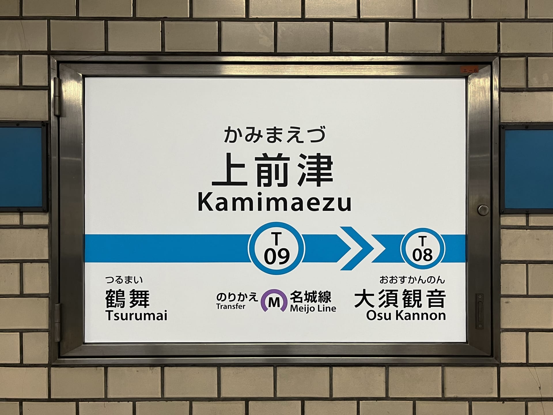 上前津駅 (T09) のタイル張りの壁に鶴舞 (T08) と大須観音への行き方を示す標識があり、近くにある乗り換えオプションがあり、上前津へ向かう通勤者や韓国語教室マンツーマンセッションに参加する人に最適です。.