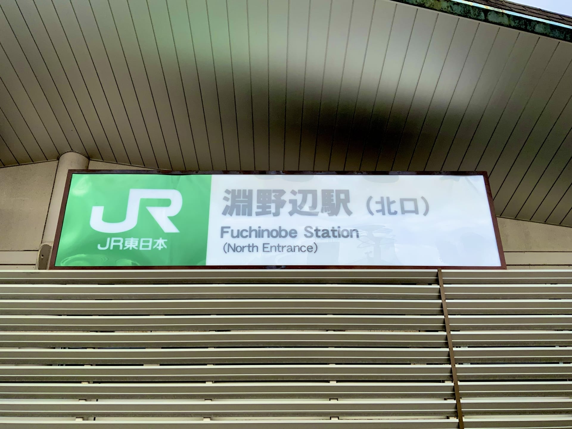 淵野辺駅北口の標識。モダンな建築を背景に、英語と日本語の文字が入った JR 東日本のロゴが描かれています。近くの韓国語教室マンツーマンでは、言語愛好家向けに個別の韓国語レッスンを提供しています。.