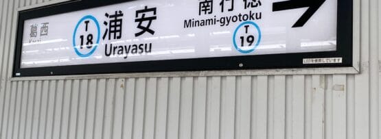 地下鉄内で浦安駅 (T 18) と南行徳 (T 19) の方向を示す標識。浦安近くにあるマンツーマンの韓国語教室のカラフルな広告によって美しく強調されています。.