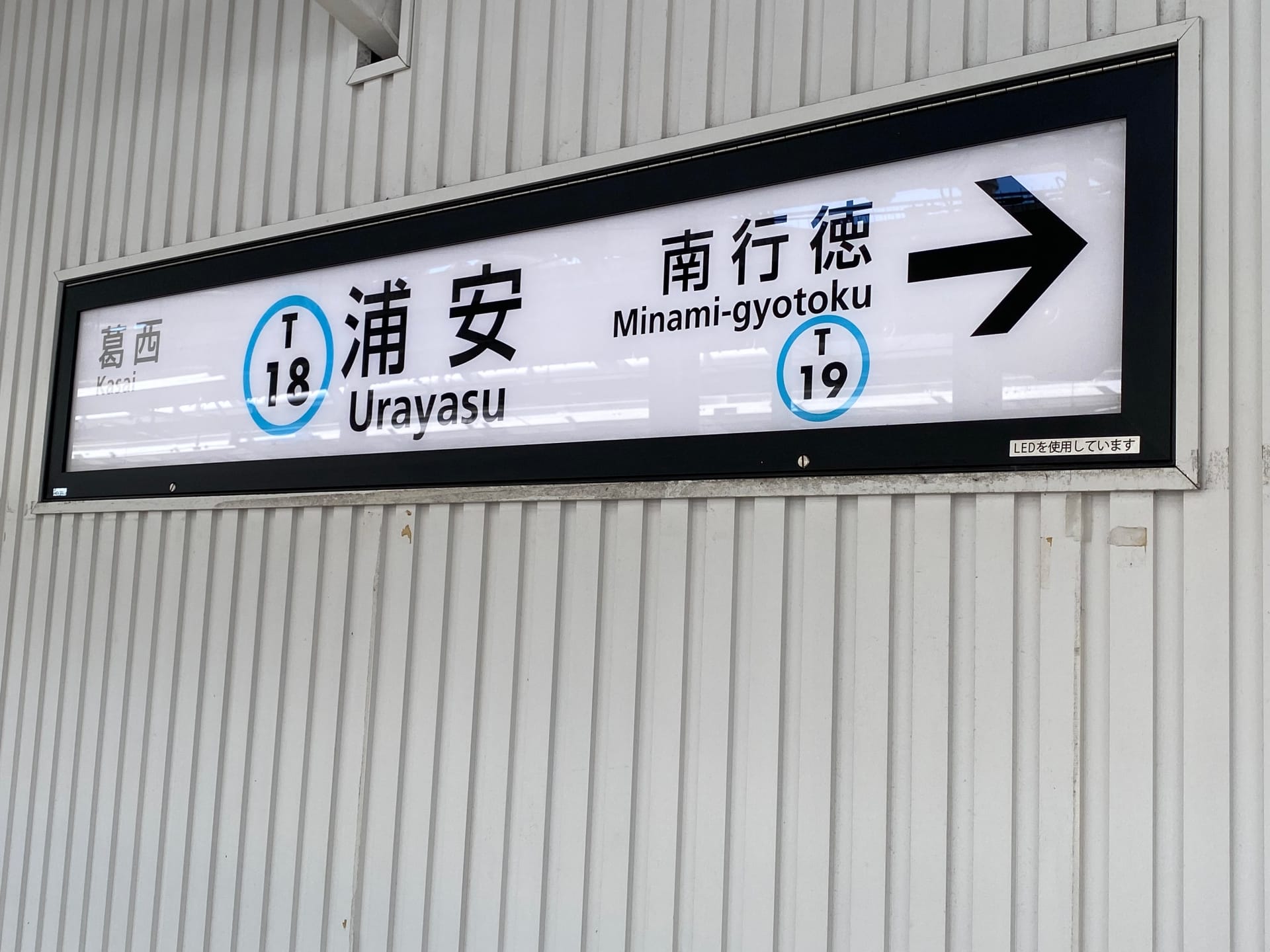 地下鉄内で浦安駅 (T 18) と南行徳 (T 19) の方向を示す標識。浦安近くにあるマンツーマンの韓国語教室のカラフルな広告によって美しく強調されています。.