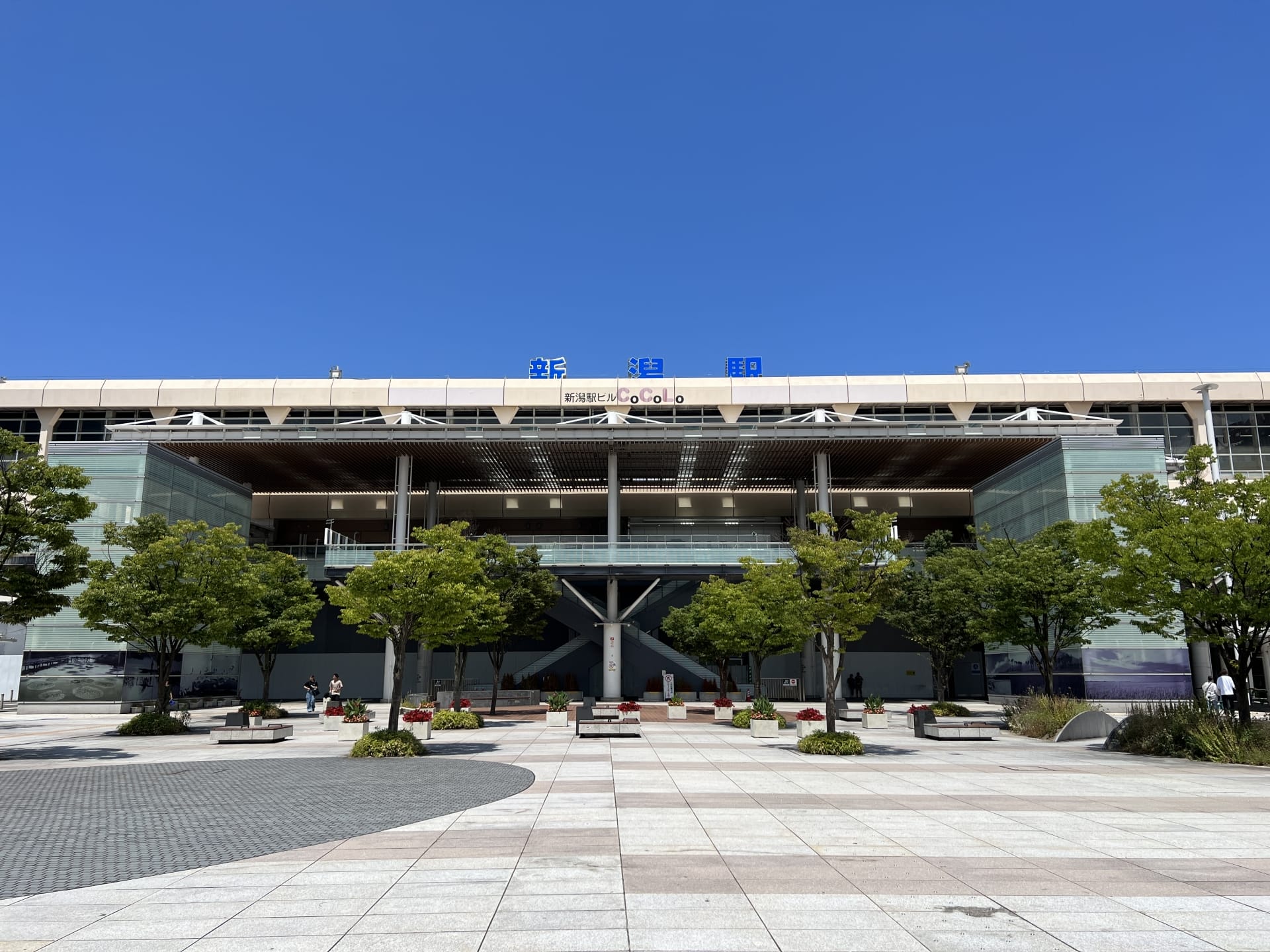 新潟の青空とモダンな建物の外観。前景には木々やベンチがあり、勉強したり、近くの韓国語教室マンツーマンでの授業後にリラックスしたりするのに最適な場所です。.