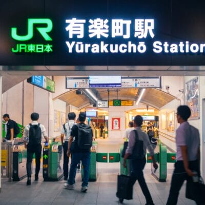 有楽町駅の改札を通る人々。上の駅名標は日本語とローマ字が併記されて点灯しています。近くの韓国語教室マンツーマンでは、マンツーマンで韓国語を学びたい人向けに個別の言語レッスンを提供しています。.