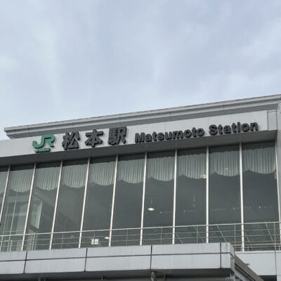 この画像は松本駅の外観を捉えたもので、日本語と英語の標識が掲げられており、韓国語教室マンツーマンに見られる個人的な配慮に似た活気に満ちた文化の融合を反映しています。.