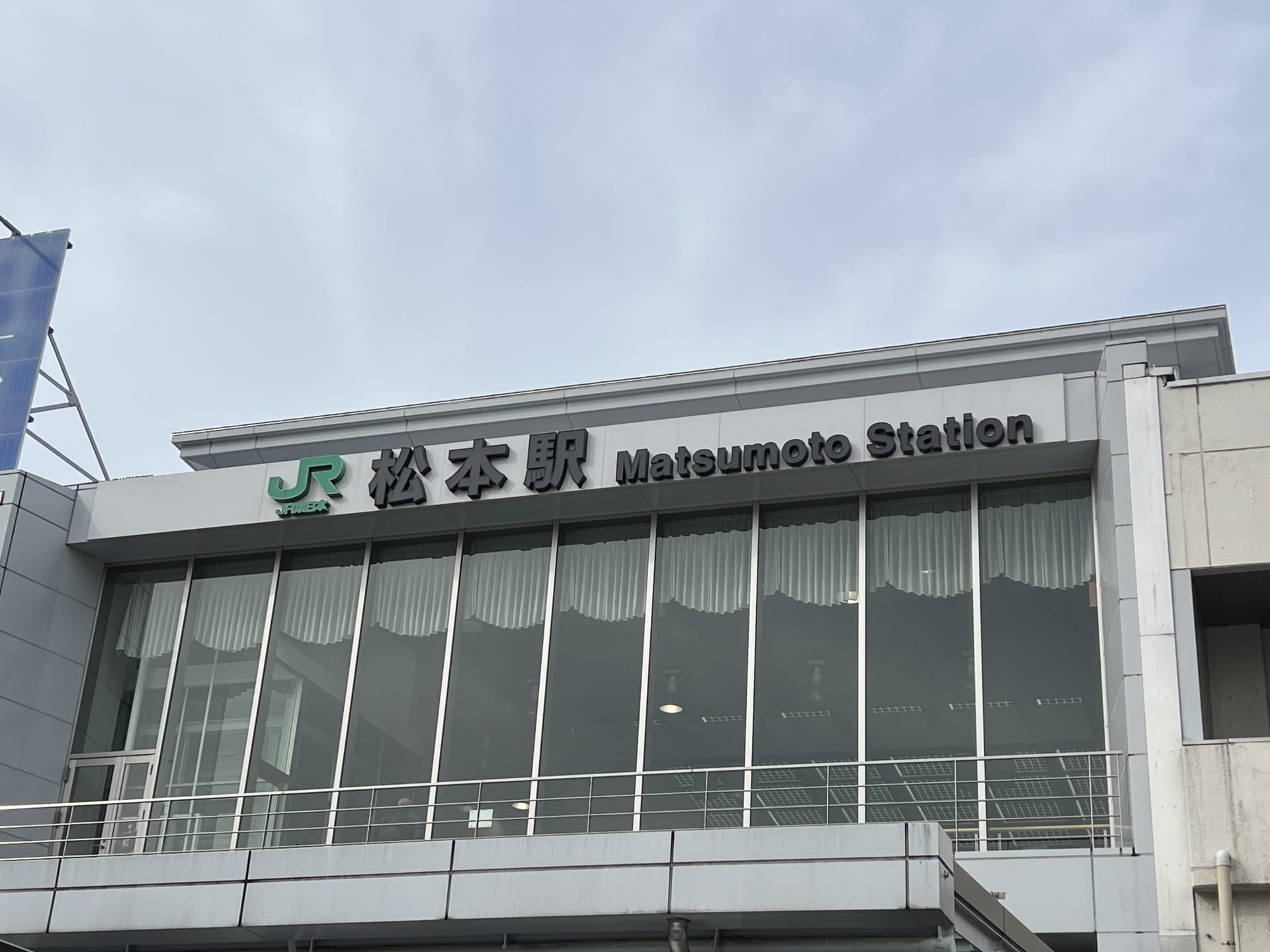 この画像は松本駅の外観を捉えたもので、日本語と英語の標識が掲げられており、韓国語教室マンツーマンに見られる個人的な配慮に似た活気に満ちた文化の融合を反映しています。.