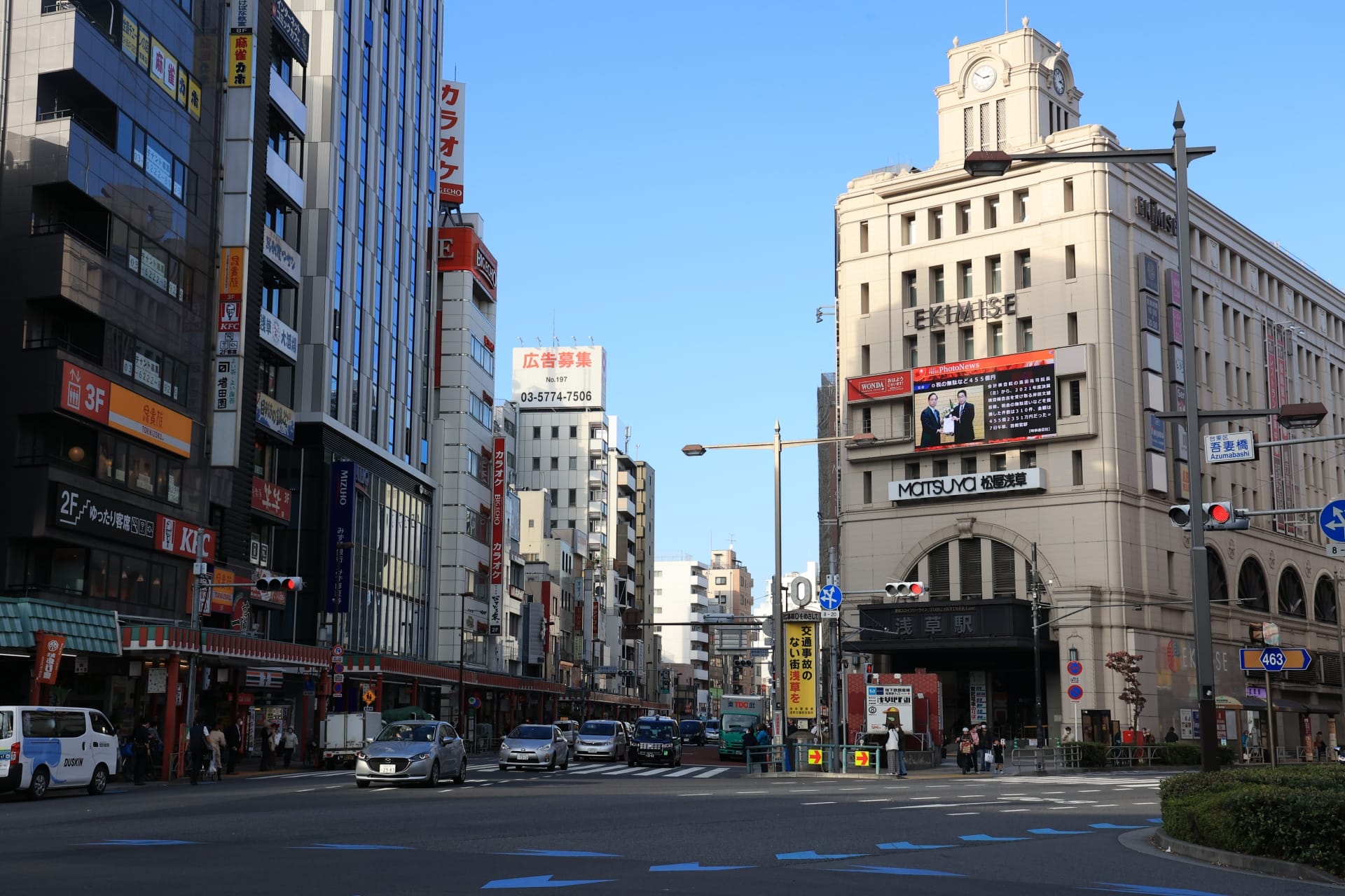 にぎやかな浅草の繁華街の交差点。車や歩行者が人混みを縫うように行き交い、日本語の看板や広告が飾られた高層ビルに囲まれている。頭上には澄んだ青空が広がり、近くには韓国語教室マンツーマンが学習者を招き入れます。.