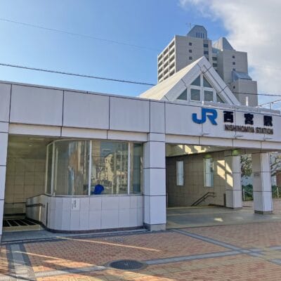 JR西宮駅の入口。一面ガラス張りの白い建物が特徴。曇り空の下、背景に高層ビルが見え、近くにある個人向けの韓国語教室マンツーマンのような活気に満ちた文化と多様な機会を反映しています。.