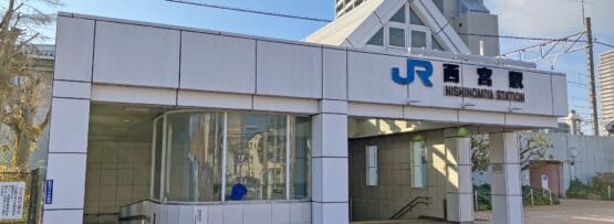 JR西宮駅の入口。一面ガラス張りの白い建物が特徴。曇り空の下、背景に高層ビルが見え、近くにある個人向けの韓国語教室マンツーマンのような活気に満ちた文化と多様な機会を反映しています。.