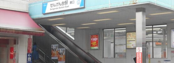 せんげん台駅東の入り口にはエスカレーターと階段があり、目に見える建物に囲まれた日本語の看板が設置されています。近くには、個人に合わせた語学学習を提供する韓国語教室マンツーマンがあります。.