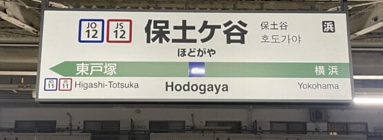 保土ヶ谷の駅名標は日本語と英語で表示され、東戸塚と横浜への方向が記載されており、駅コードは JO12 と JS12 です。韓国語教室マンツーマンやその他の目的地へ向かう通勤者に最適です。.