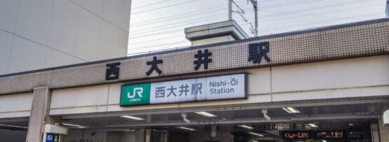 西大井駅の入口には日本語と英語の標識が設置されています。人々が行き交い、近くの韓国語教室マンツーマンへ向かう人もおり、都市部の活動と教育活動が融合しています。.