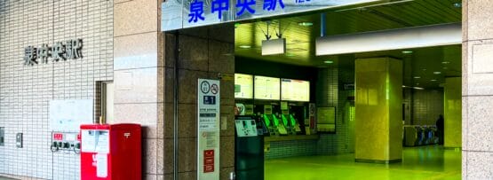 泉中央駅の入り口。近くに券売機と赤い郵便ポストがあります。入り口の上には日本語と英語の標識があります。.