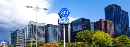 日本の東京にある内堀通り 301 の道路標識は大手町を指しており、部分的に曇った空の下、背景には高層ビルと緑が広がっています。.