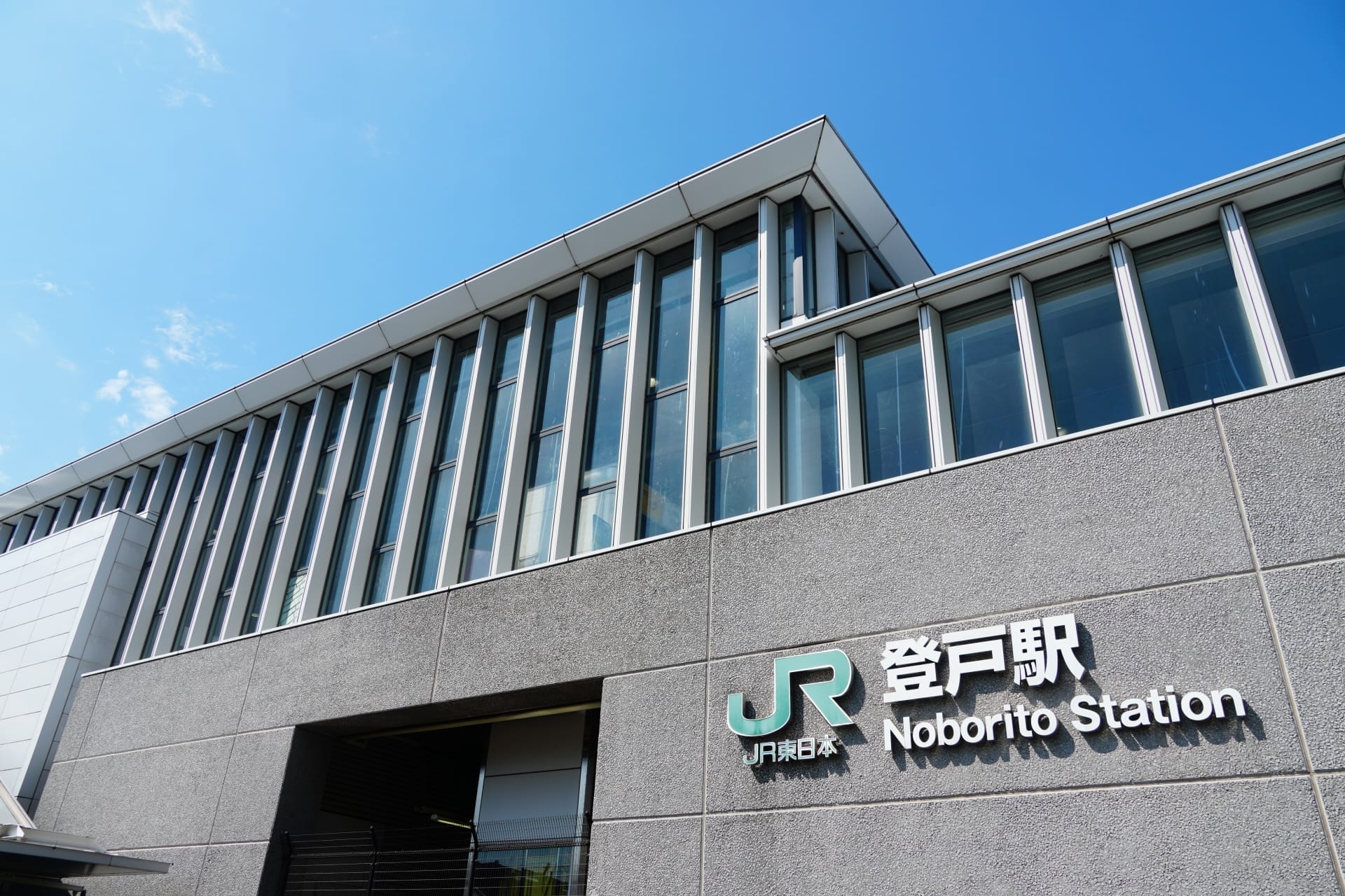 快晴の青空の下、JRロゴが目印の登戸駅の外観。一日を始めるのに最適な場所です。また、近くの韓国語教室マンツーマンに行き、個人に合わせた言語学習をするのにも最適です。.