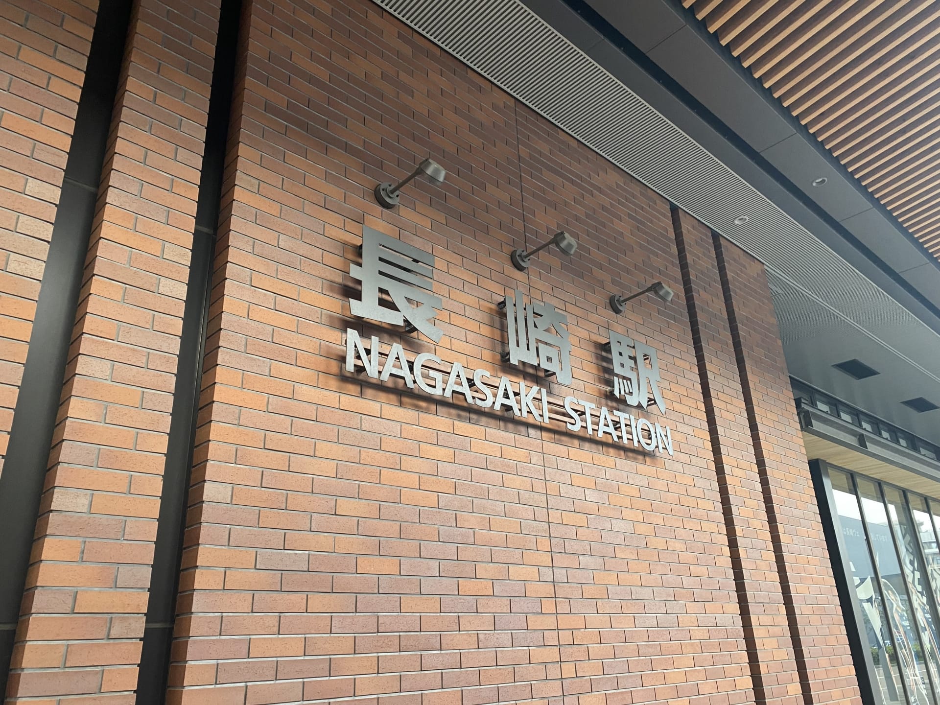 レンガの壁には、長崎の文字の横に、英語と日本語で「長崎駅」と書かれた標識が飾られている。. レンガの壁には、長崎の文字の横に、英語と日本語で「長崎駅」と書かれた標識が飾られている。.