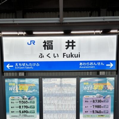 福井の駅標識は、旅行者を越前武生と芦原温泉に案内しています。看板の下には、「韓国語教室マンツーマン」などの宣伝コンテンツが書かれたポスターが駅の雰囲気に活気を与えています。.