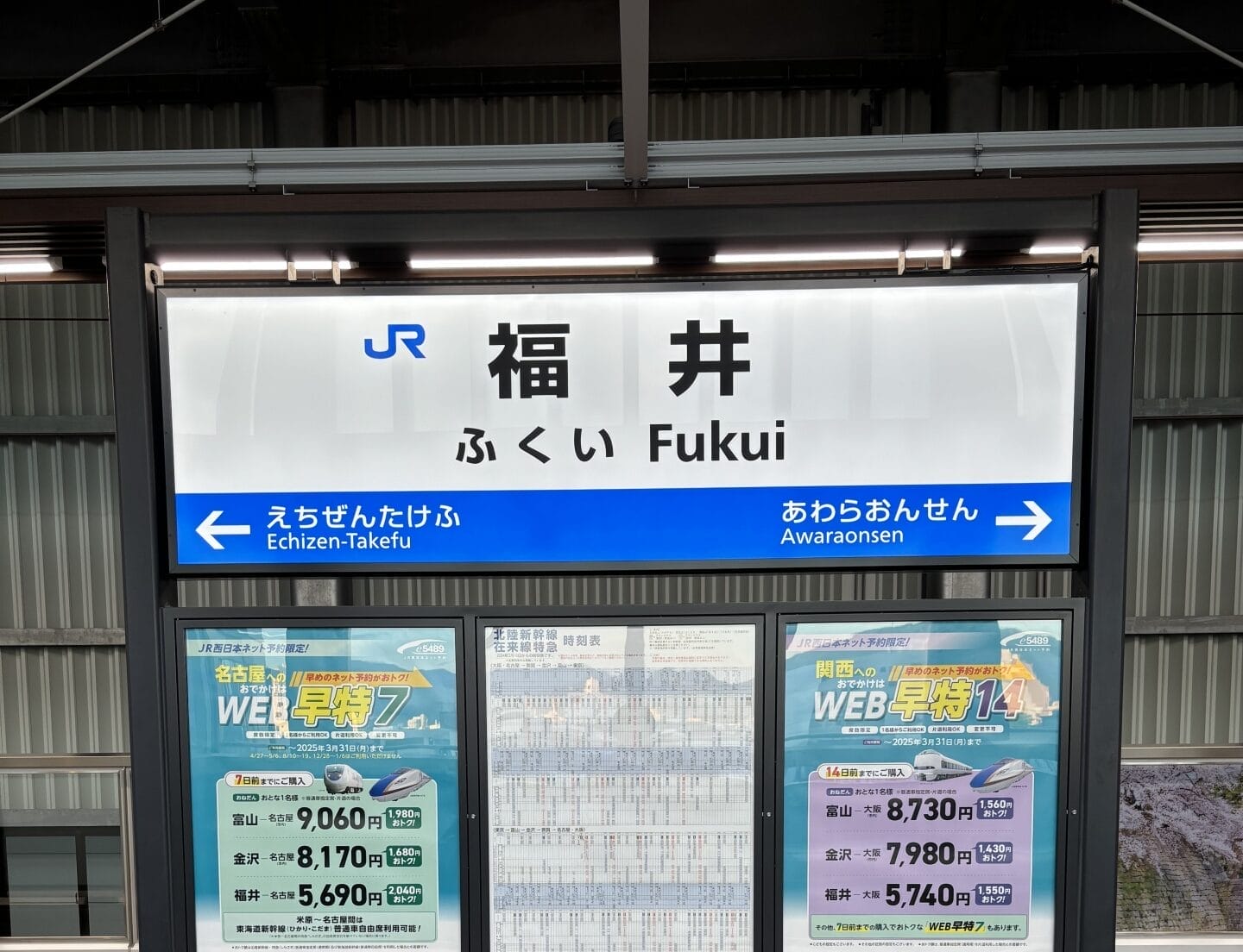 福井の駅標識は、旅行者を越前武生と芦原温泉に案内しています。看板の下には、「韓国語教室マンツーマン」などの宣伝コンテンツが書かれたポスターが駅の雰囲気に活気を与えています。.