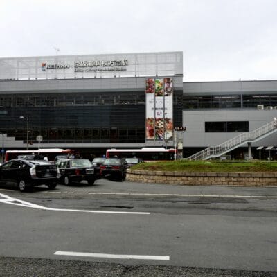 枚方市にある近代的な鉄道駅の外観。前をバスや車が通過し、ポールには時計があり、日本語と英語の文字が書かれた看板が目に見える。近くには韓国語教室マンツーマンがあり、マンツーマンで韓国語を学びたい方に最適です。.