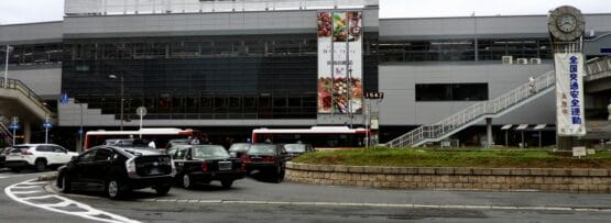 枚方市にある近代的な鉄道駅の外観。前をバスや車が通過し、ポールには時計があり、日本語と英語の文字が書かれた看板が目に見える。近くには韓国語教室マンツーマンがあり、マンツーマンで韓国語を学びたい方に最適です。.