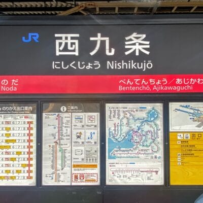 西九条の駅標識には、地図、電車の時刻表、日英二か国語の情報が誇らしげに表示されています。西九条エリアに近い便利な場所にあり、道順を探している旅行者や、近くで韓国語教室マンツーマンのセッションに参加している旅行者にわかりやすく提供します。.