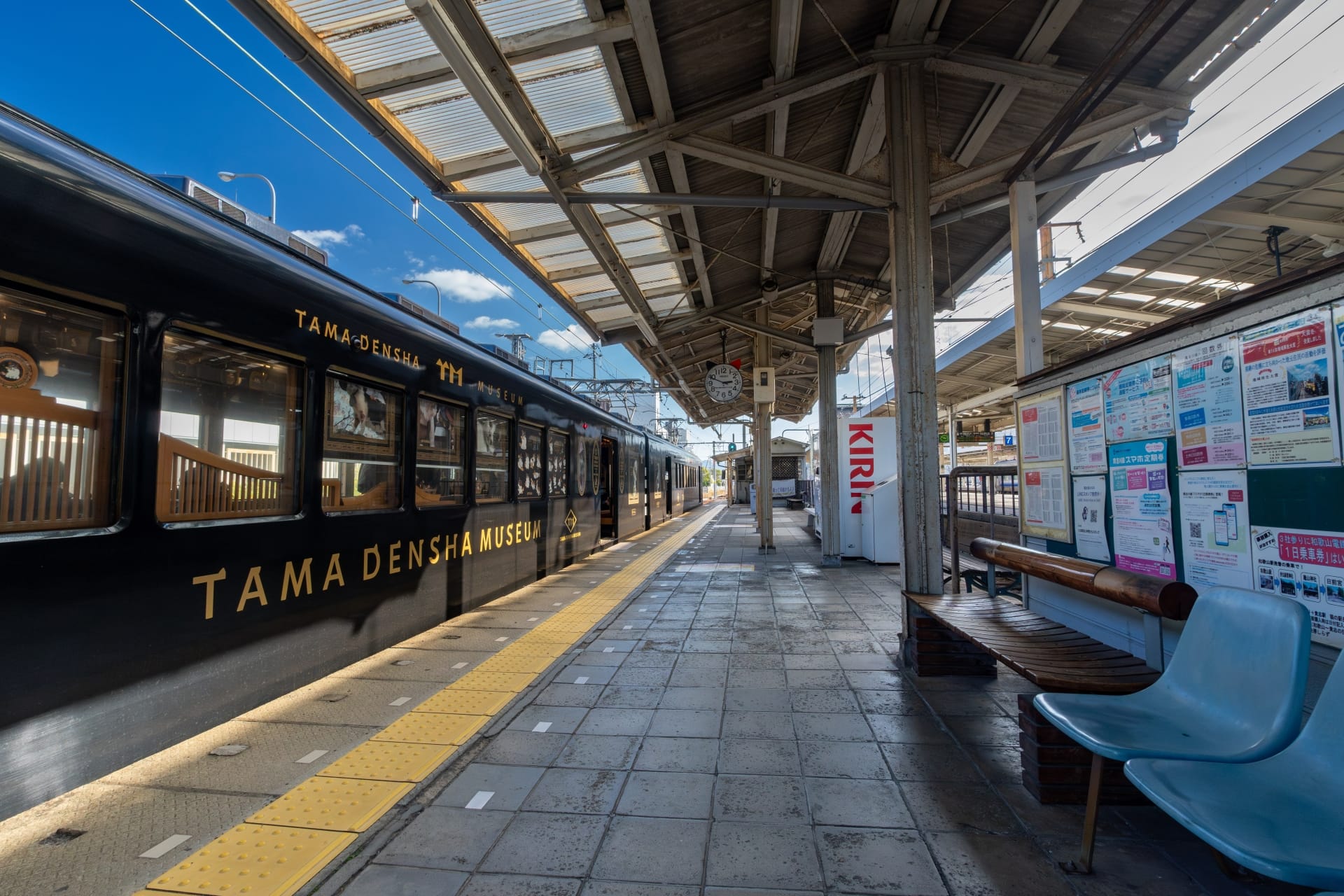 駅のホームには、左側に「たま電車ミュージアム」と書かれた黒い電車が停まっており、右側には大きなキリンの自動販売機が立っている。屋根付きの掲示板のそばには青い椅子が整然と並べられており、和歌山の穏やかな雰囲気を醸し出している。.